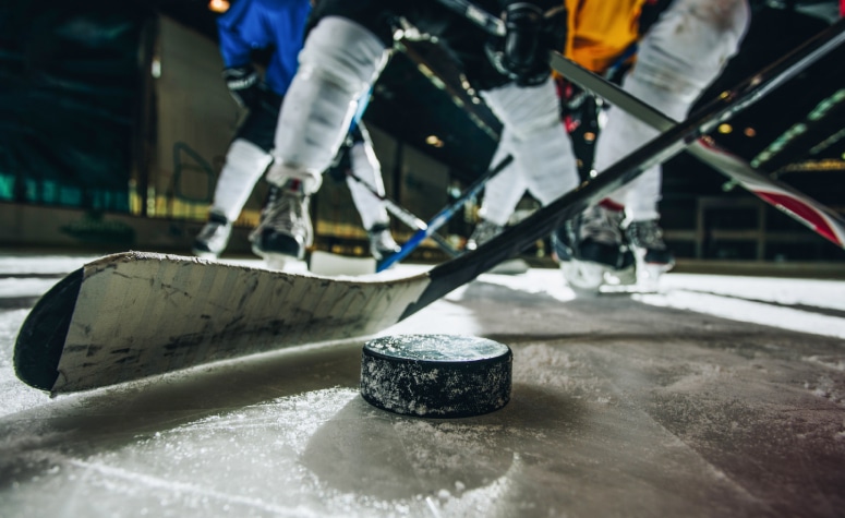 Close up of hockey puck and stick during a match with players in the background.